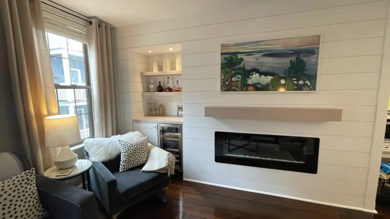 Cozy living room with armchair, fireplace, built-in shelves, window seat, and landscape painting