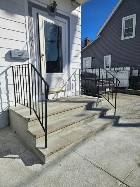 Front steps to a white house with a glass door and black railing, beside a neighboring gray house