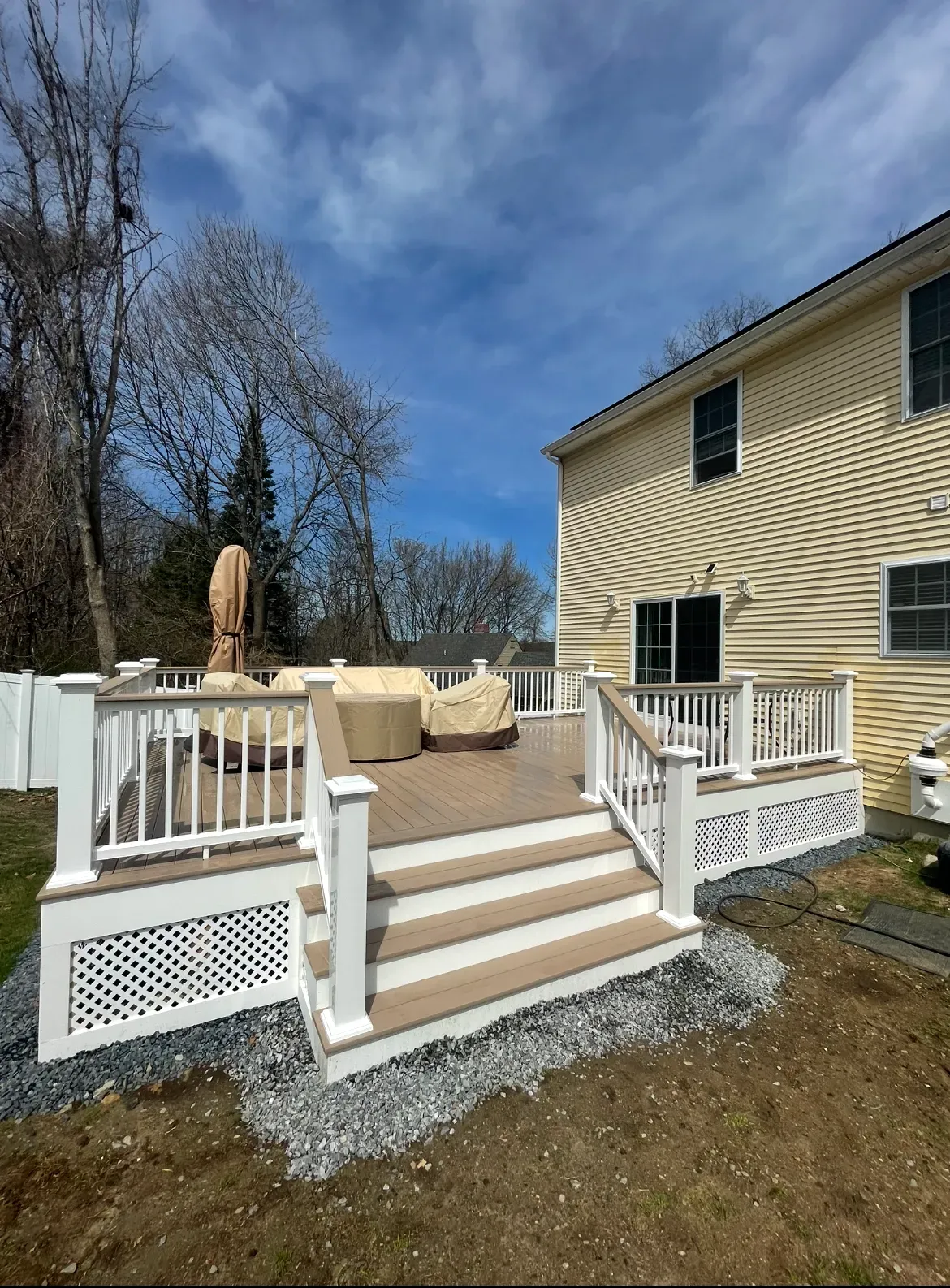 Backyard deck with white railings, tan steps, and beige house under a blue sky