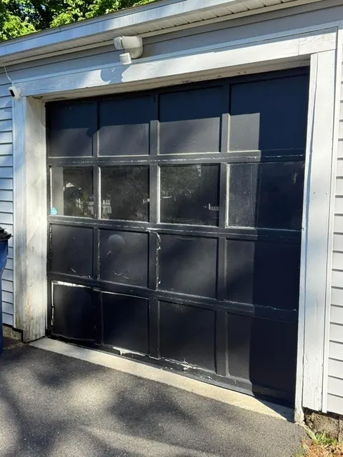 Old damaged black carriage-style garage door with peeling paint before replacement