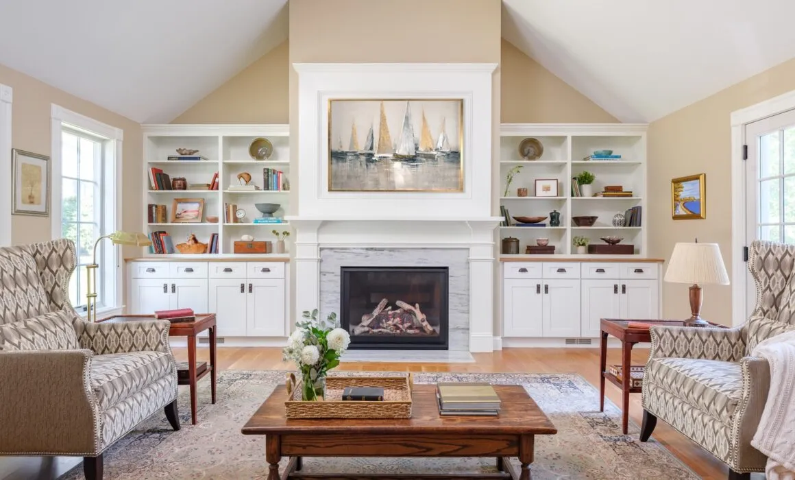 Bright, elegant living room remodel with a fireplace, built-in shelves, sailboat art, and natural light – Woodland Builders, South Shore MA.
