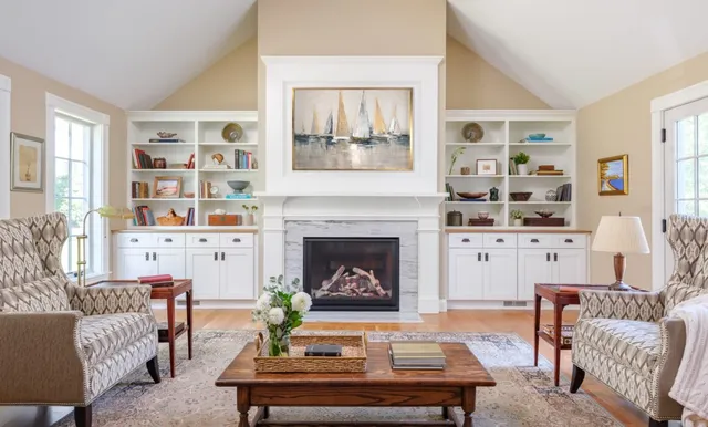 Bright, elegant living room remodel with a fireplace, built-in shelves, sailboat art, and natural light – Woodland Builders, South Shore MA.