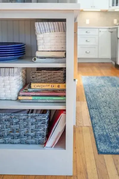 Open shelving with books and baskets beside a blue rug in a bright room
