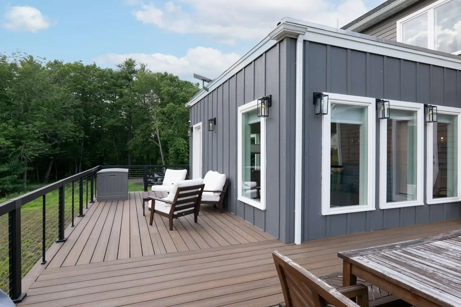 Modern custom home exterior featuring a gray facade, large windows, and a wooden deck with seating, emphasizing the design-build approach of Bradford Construction Management.