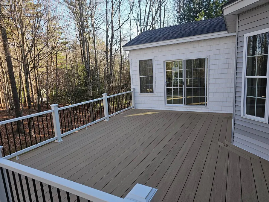 Wide-angle view of a finished deck and home addition with stairs leading down to the yard. The extension has white siding and large windows.
