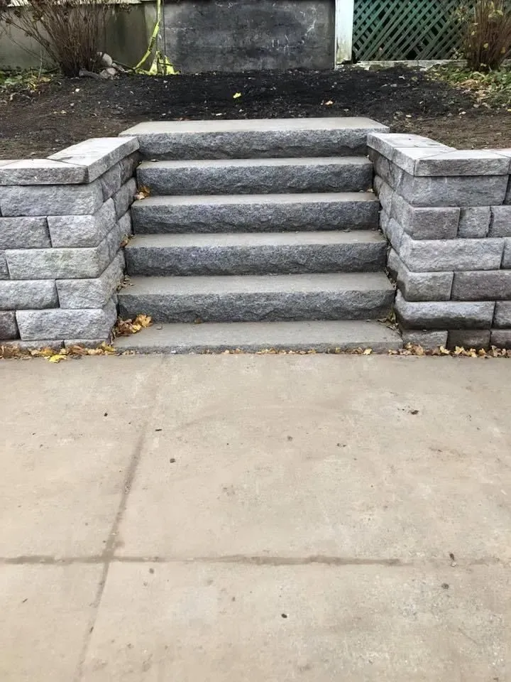 Stone steps with retaining walls leading up from a concrete sidewalk to a higher yard.