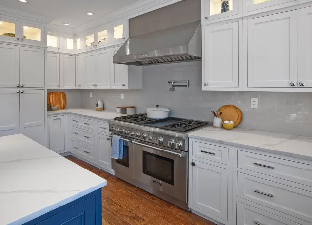 Bright modern kitchen with white cabinets, blue island, stainless steel stove, and light wood floor