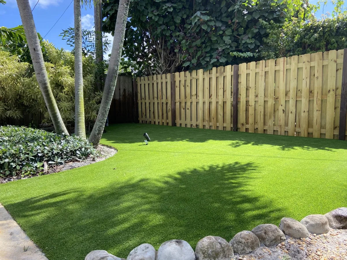 Backyard in Elk Creek, California with Global Syn-Turf Spring-50 artificial grass, surrounded by a wooden fence, palm trees, and landscaped garden
