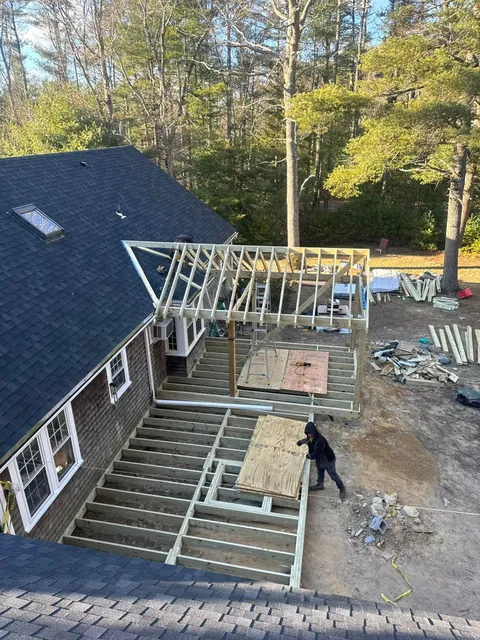 House under construction with roof framing and a worker beside a partially built deck