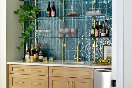 Home bar with teal tile, brass shelving, and a white stone countertop.