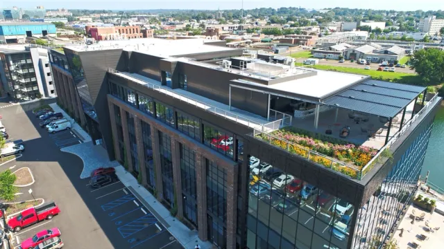 Aerial view of a modern commercial office complex with rooftop terraces — dark façade and expansive glass windows overlooking the city.