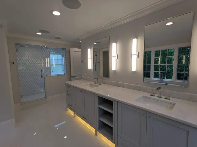 Modern bathroom with double vanity, two mirrors, vertical light fixtures, a walk-in shower with patterned glass, and a large window with lush greenery outside.