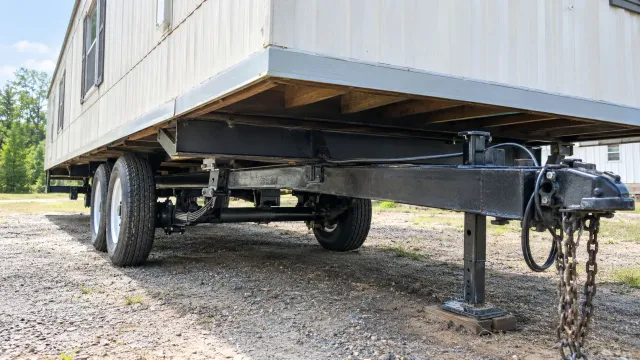 White trailer with dual axles and front jack stands on gravel, viewed from underneath the side.