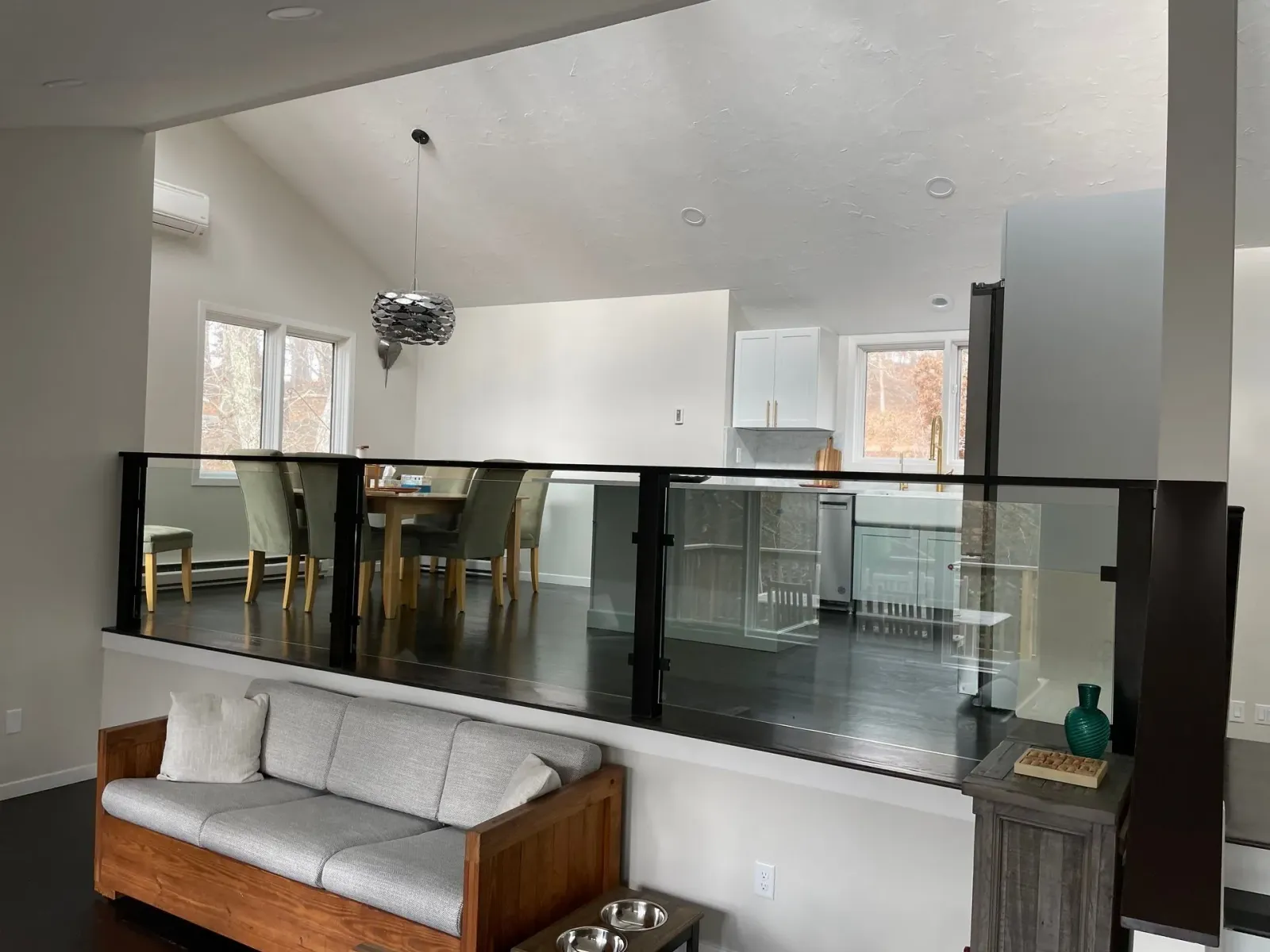 Open-concept interior with glass railing overlooking dining area and kitchen.  Sofa in foreground, dark wood floors.