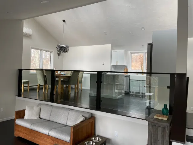 Open-concept interior with glass railing overlooking dining area and kitchen.  Sofa in foreground, dark wood floors.