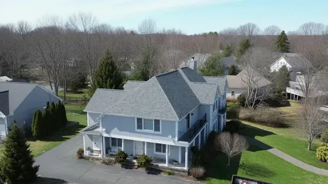 Aerial view of a light blue suburban house with a gray roof and surrounding trees in a quiet neighborhood