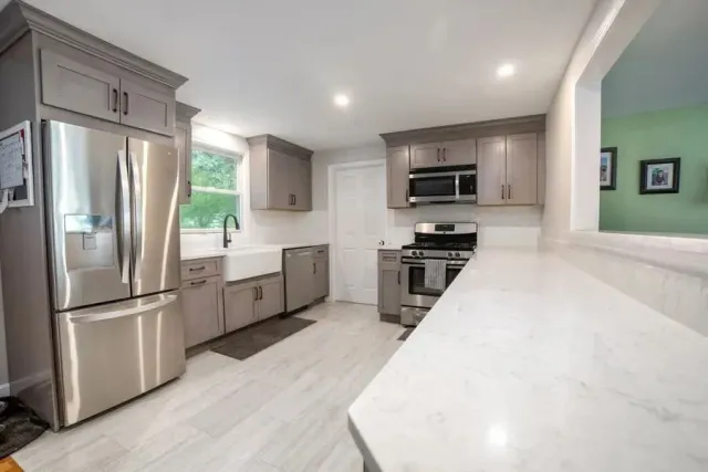 Bright modern kitchen with stainless steel appliances, gray cabinets, white counters, and a pass-through opening