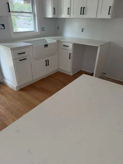 Bright white kitchen with cabinets, countertop, window, and wood floor