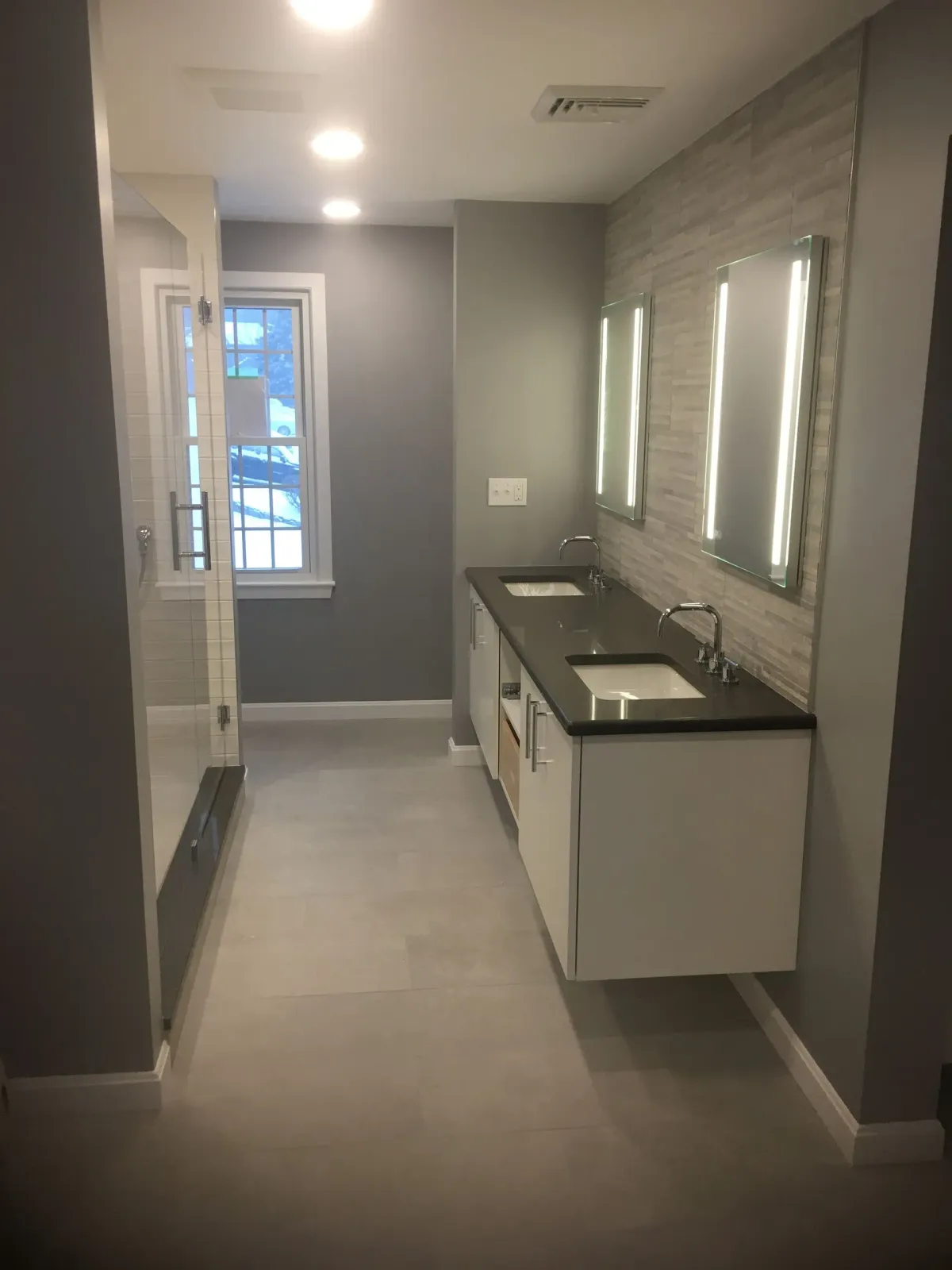 A bathroom with two sinks , a shower and a window.