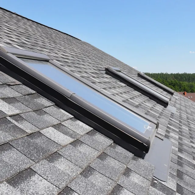 Solar roof skylights on a gray shingled roof under a clear blue sky.