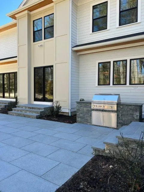 Modern house exterior with patio pavers, white brick walls, black-framed windows, and a stainless grill