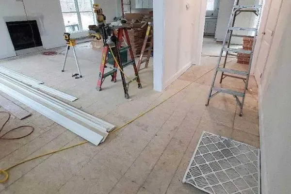 an active home renovation construction site featuring a subfloor, ladders, tools, and trim, prior to hardwood floor installation and buffing