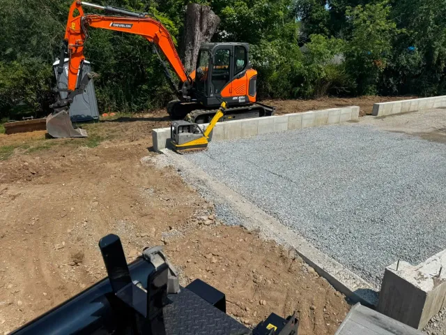 Excavator and compactor beside a prepared foundation gravel base