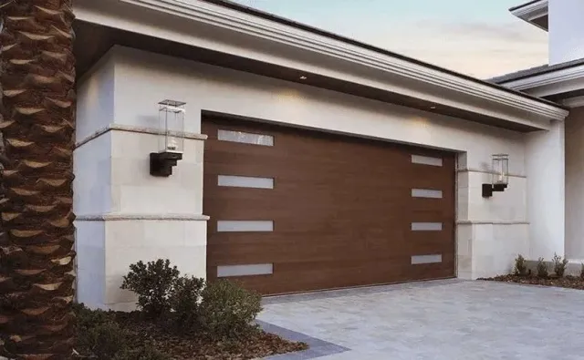 Modern brown garage door with rectangular glass panels; stucco exterior with palm tree.