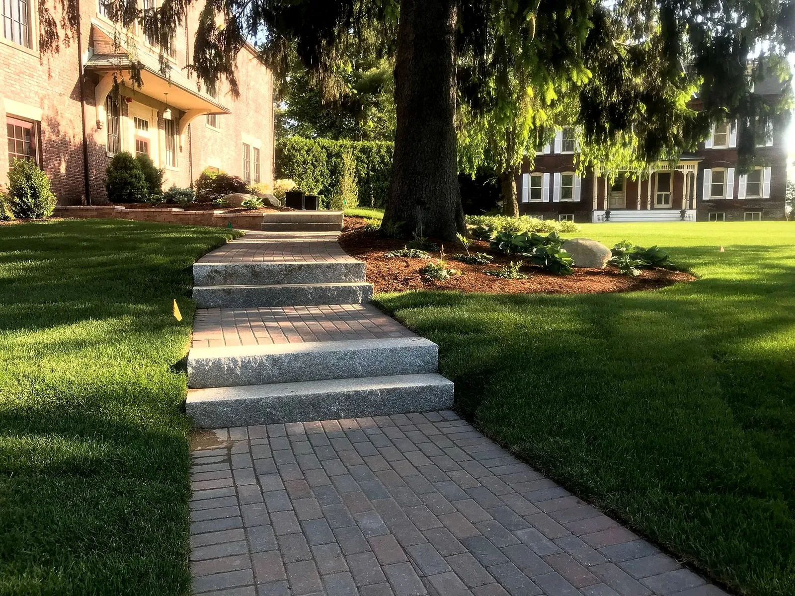 Brick pathway and stone steps leading up to two brick buildings, surrounded by green lawns and trees.