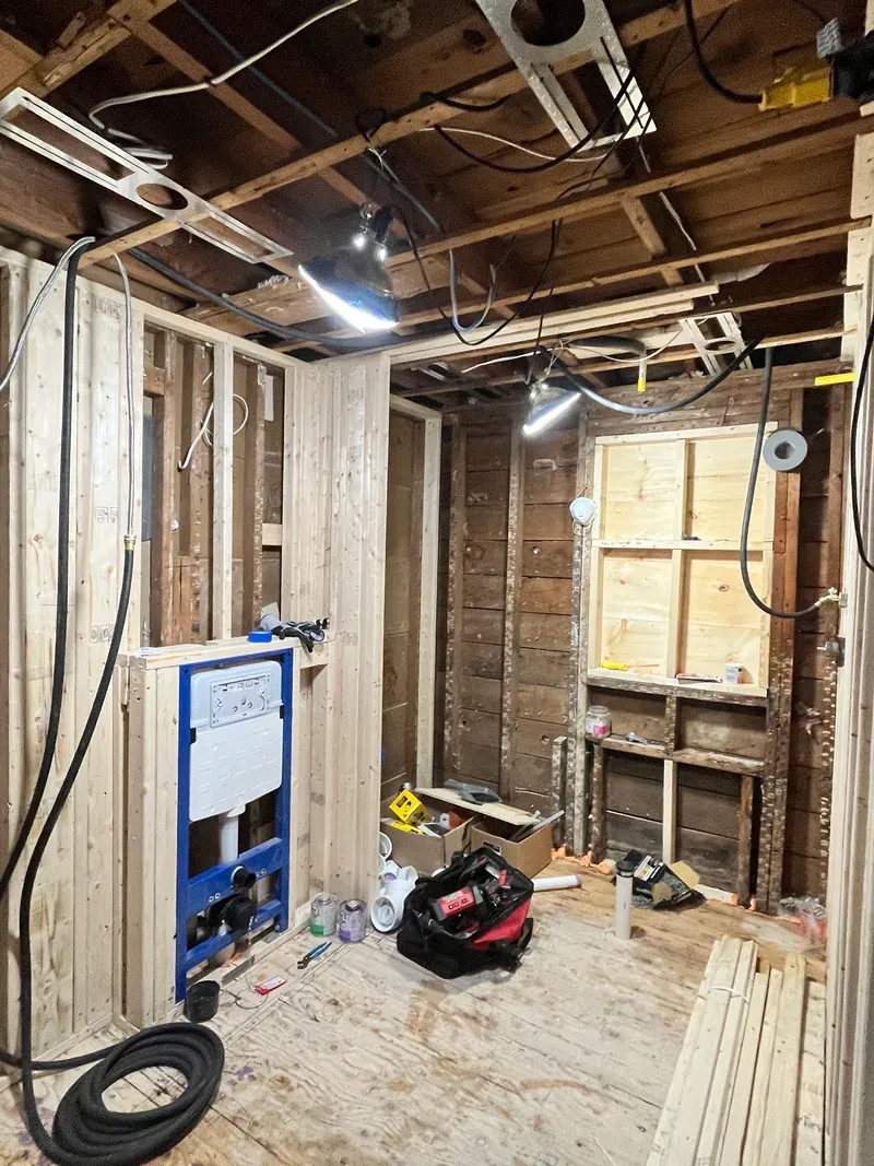 Natick bathroom stripped to studs and joists with the wall-hung toilet carrier blocked and braced