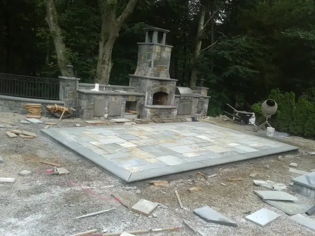 Outdoor kitchen and stone fireplace under construction on a bluestone patio