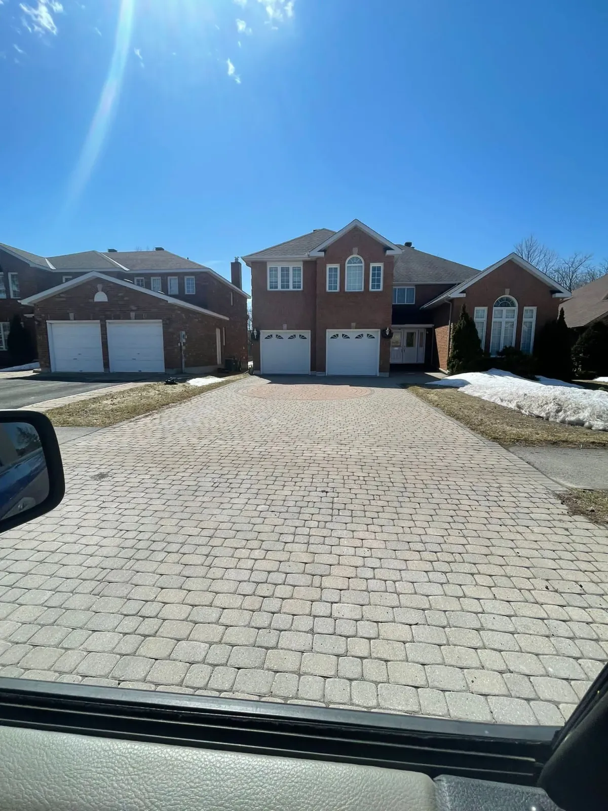 A brick driveway leads to a two-story house with a red brick facade on a sunny day.