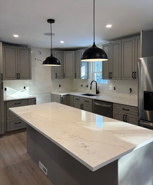 Modern kitchen with gray cabinets, marble island, white countertops, and black pendant lights