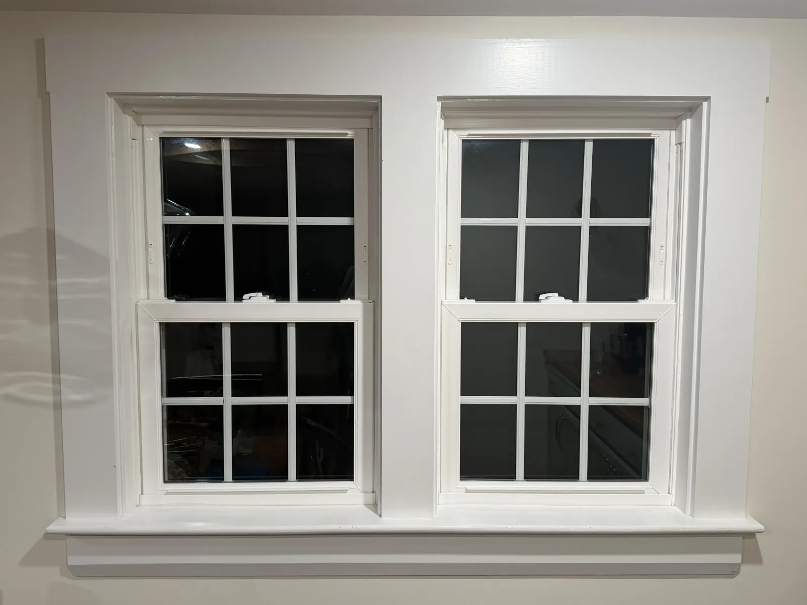 A double window with white frames and grid patterns, set in a light-colored wall.