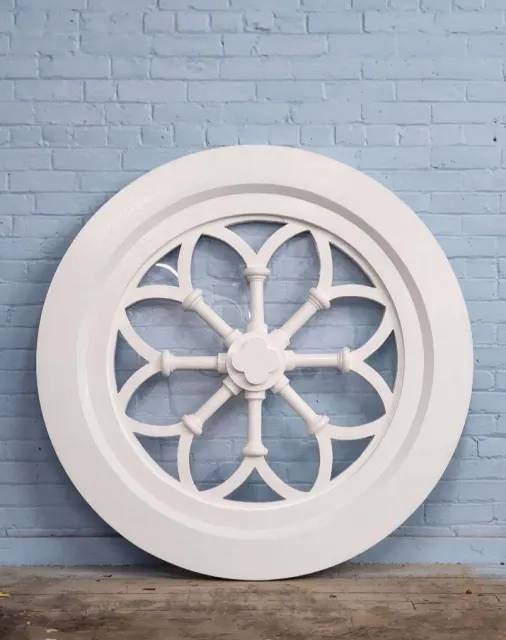 Large white decorative wheel or clock with a radial pattern, leaning against a light blue brick wall.