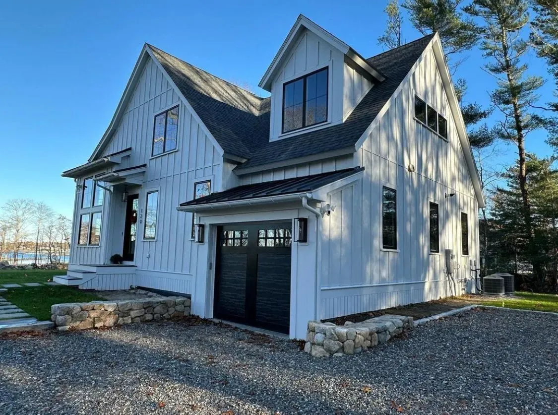 A white house with a black garage door and a black roof