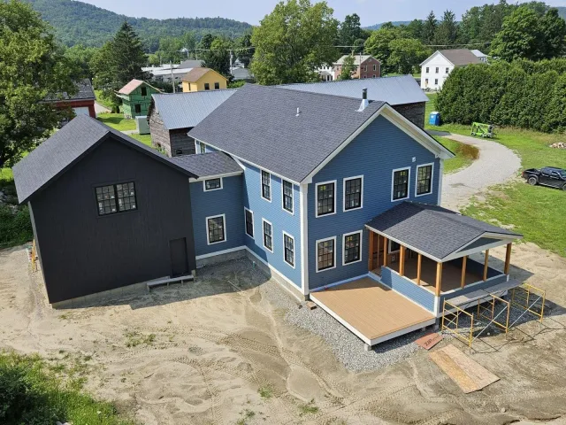 A photo of a large blue house with white trim, a porch, and a black attached garage. The photo is taken from an aerial view. The village of Richmond is visible in the background.