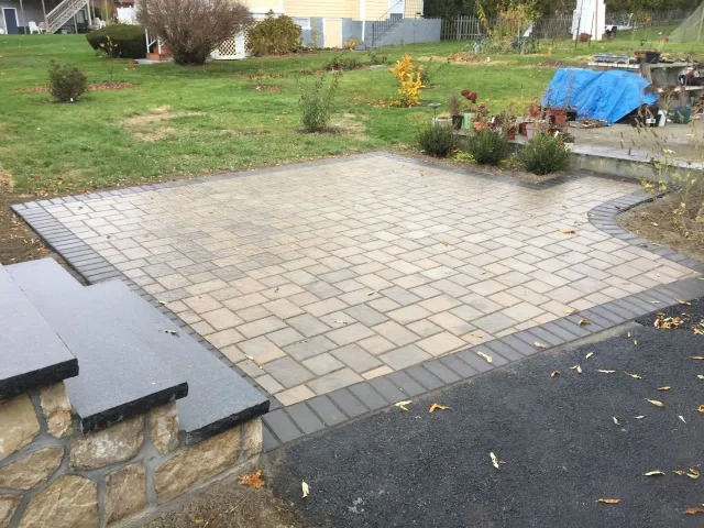 A brick patio with stairs leading up to it in a backyard.
