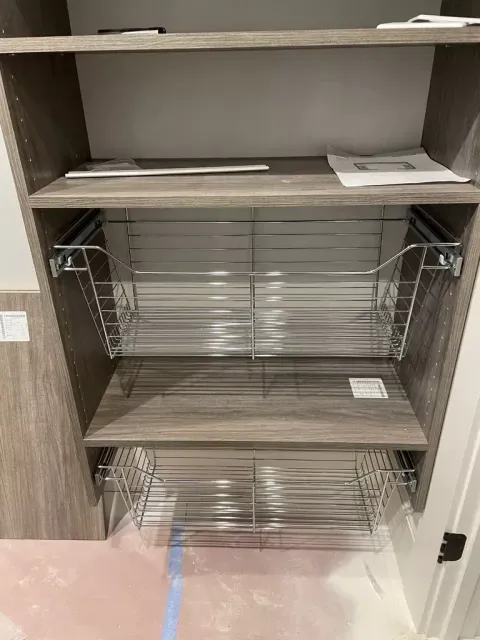 Empty wood cabinet with wire pull-out shelves and a lower drawer in a kitchen or bathroom nook