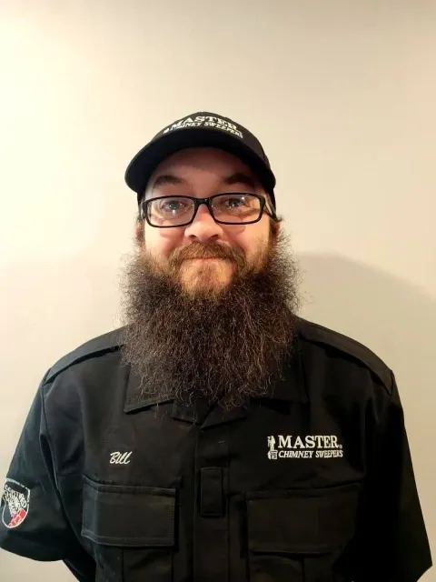 A man with a beard and glasses is wearing a hat and a black shirt.