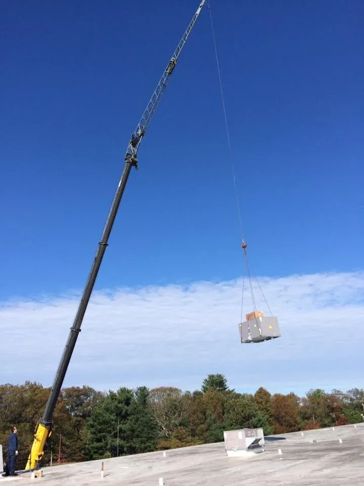 Crane lifting an HVAC unit onto a rooftop with clear blue sky background.
