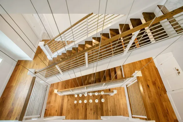 From the top view of a staircase, showing wooden steps, white railing, and a modern chandelier hanging from the ceiling with multiple bulbs.