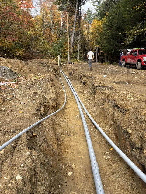 Two runs of gray PVC conduit laid along a long open trench toward the work truck