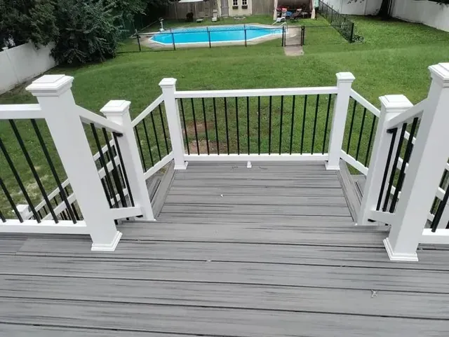 Grey deck with white railing and black spindles, looking out to a backyard with a pool.