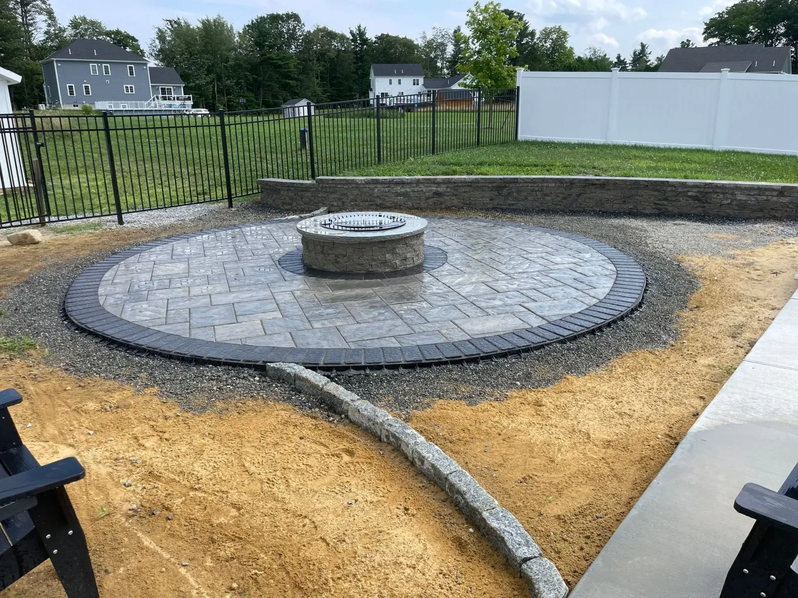 Circular stone patio with central fire pit and curved border in a landscaped yard