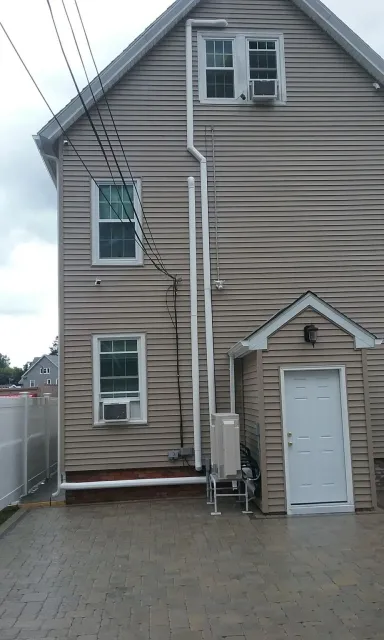 Side view of a two-story house with tan siding and a small attached garage, featuring windows and power lines.