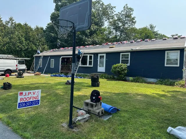 A blue house with roofing work in progress. A basketball hoop stands in front.