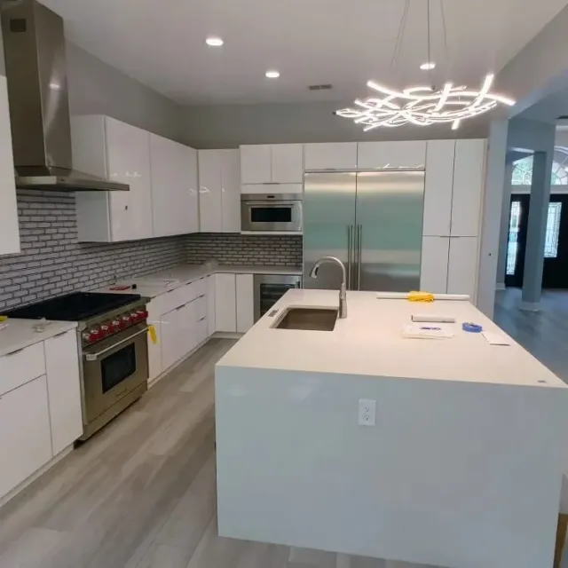 Modern kitchen with white cabinets, stainless appliances, gray backsplash, and a large island with sink and pendant light