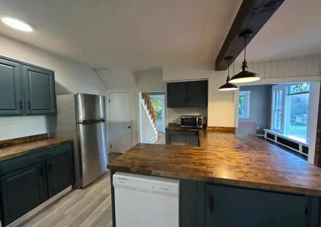 Kitchen with dark green cabinets, wooden countertops, a stainless steel refrigerator, microwave, and a window with a view of the backyard.