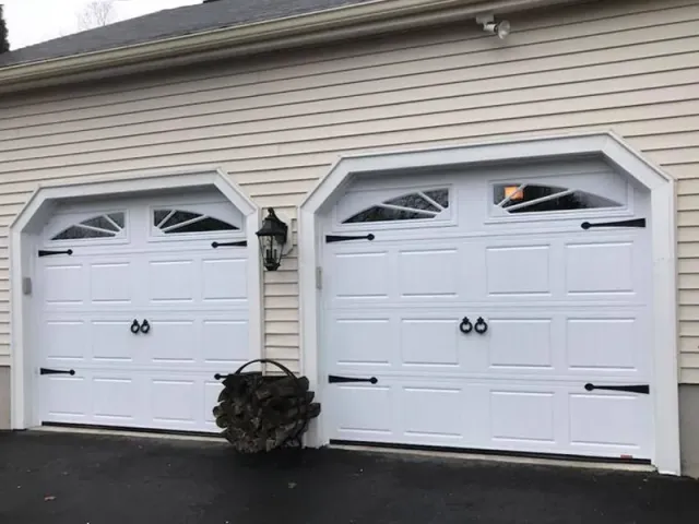 Two white garage doors are sitting next to each other on the side of a house.